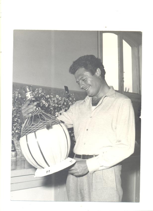 Ein Mann betrachtet lächelnd eine traditionelle Bastflasche Wein.