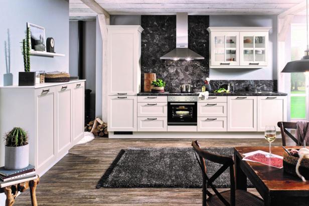 Eine moderne Landhausküche mit weißen Schränken und einem Holztisch im Vordergrund.