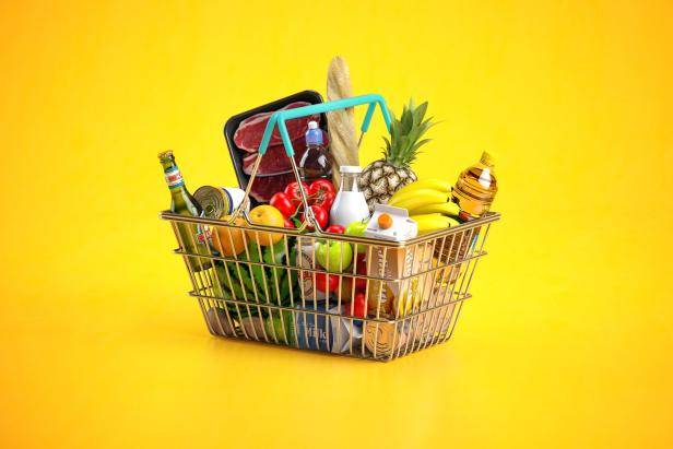 Ein Einkaufskorb gefüllt mit Lebensmitteln wie Fleisch, Obst, Gemüse und Getränken vor einem gelben Hintergrund.