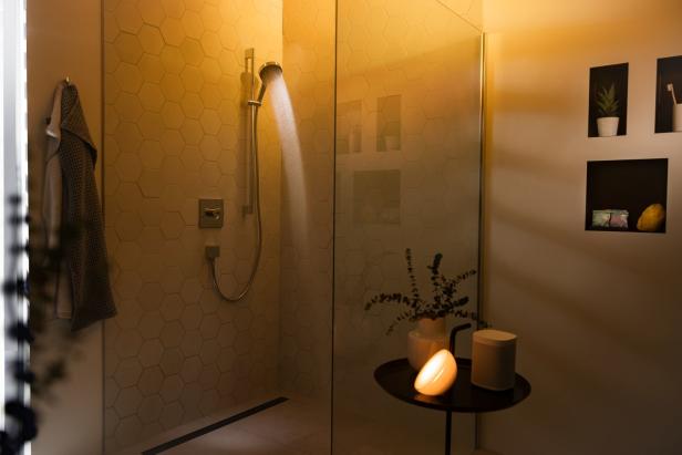 Eine Dusche mit hexagonalen Fliesen und einer eingeschalteten Lampe auf einem Tisch.
