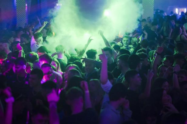 Eine Menschenmenge tanzt in einem Nachtclub mit grünen und violetten Lichtern.