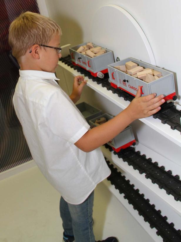 Ein Junge spielt mit einer Spielzeugeisenbahn und belädt die Waggons mit Holzklötzen.