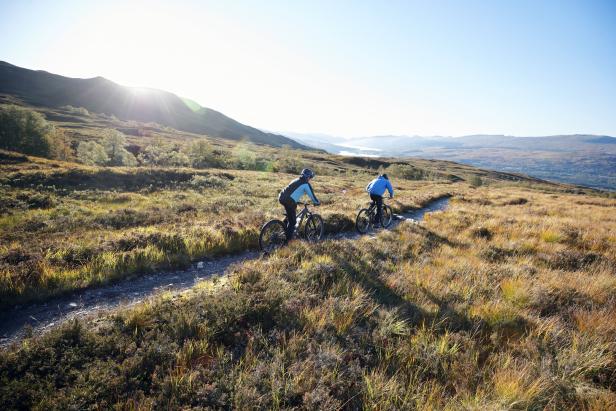Zwei Mountainbiker fahren auf einem Pfad durch eine hügelige Landschaft.