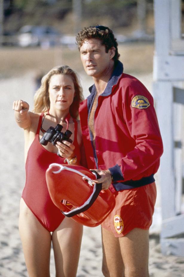 David Hasselhoff und eine Rettungsschwimmerin am Strand, sie zeigt auf etwas in der Ferne.
