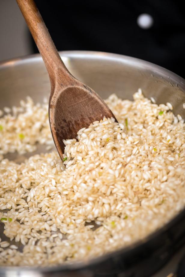Ein Holzlöffel rührt Risotto in einem Topf.