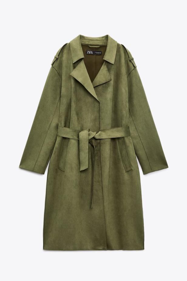 Ein olivgrüner Trenchcoat mit Bindegürtel vor einem weißen Hintergrund.