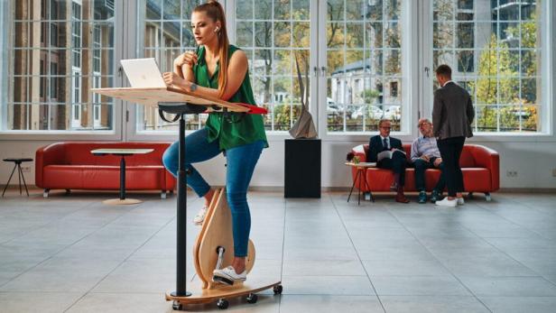 Eine Frau arbeitet an einem Laptop auf einem Schreibtischfahrrad in einem Büro.