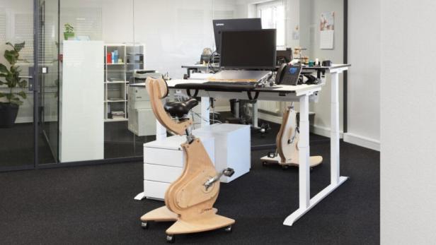 Ein höhenverstellbarer Schreibtisch mit einem integrierten, hölzernen Fahrradergometer in einem Büro.