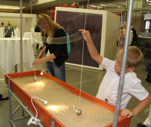 Ein Junge und eine Frau beobachten Pendel, die Muster in Sand zeichnen.