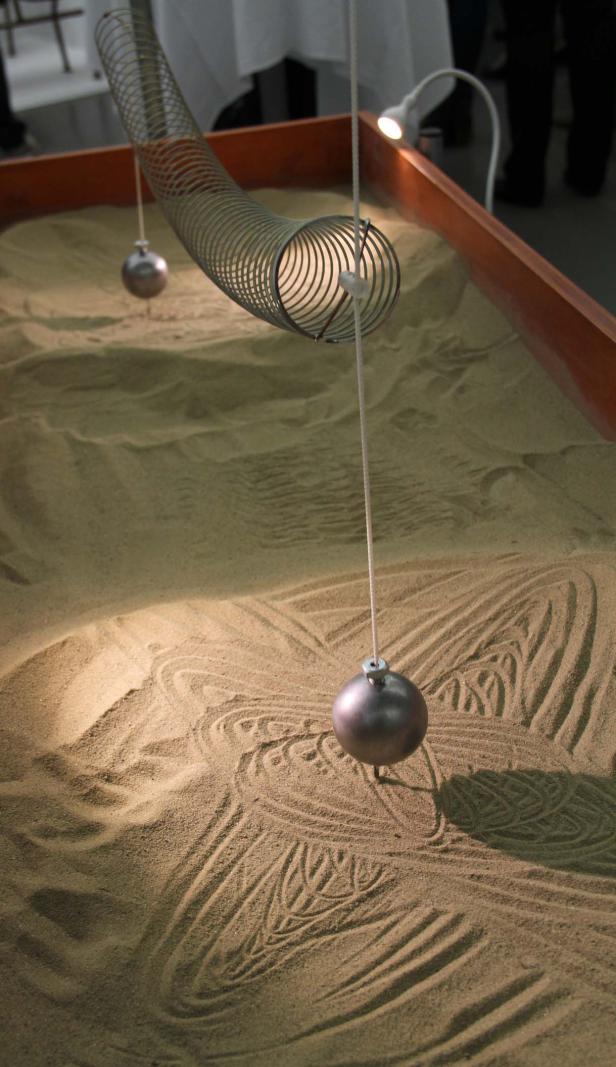 Eine Pendel zeichnet Muster in den Sand eines Zen-Gartens.