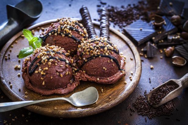 Drei Kugeln Schokoladeneis mit Nüssen und Schokoladensoße auf einem Holzbrett.