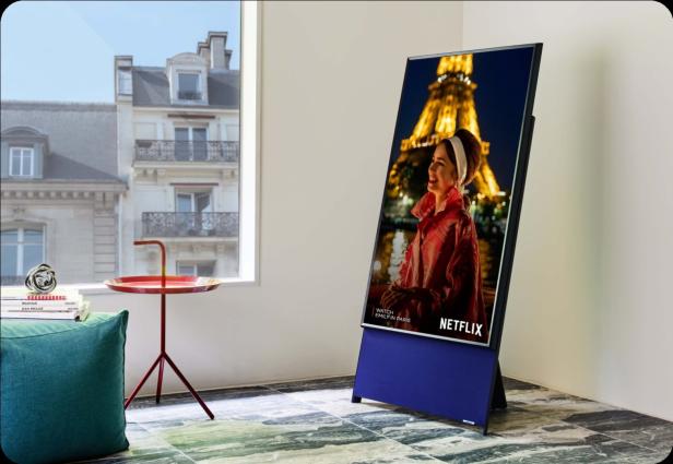 Auf einem Fernseher läuft eine Szene aus der Serie „Emily in Paris“ vor dem Eiffelturm.