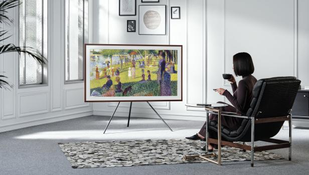 Eine Frau sitzt in einem Sessel und betrachtet ein Gemälde von Georges Seurat auf einem Fernsehgerät.