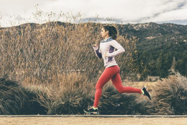 Eine Frau joggt in Sportkleidung vor einer Hügellandschaft.