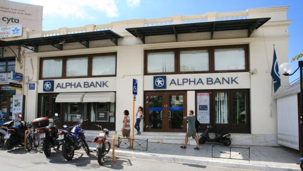 Das Gebäude der Alpha Bank mit Passanten und geparkten Motorrädern davor.