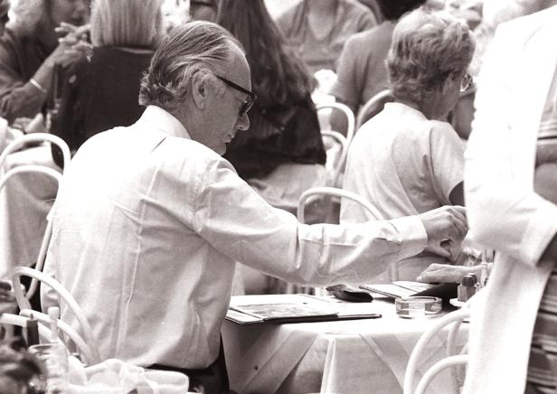 Ein Mann mit Sonnenbrille sitzt in einem Straßencafé an einem Tisch.