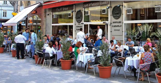 Ein belebtes Straßencafé „Zum Schwarzen Kameel“ mit vielen Gästen an Tischen.