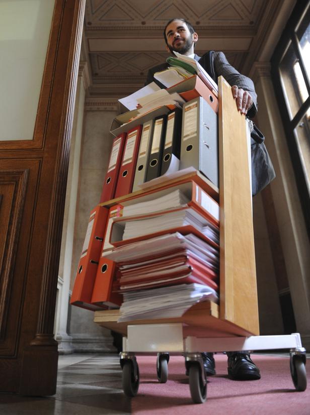 Ein Mann schiebt einen Wagen voller Aktenordner und Papierstapel.