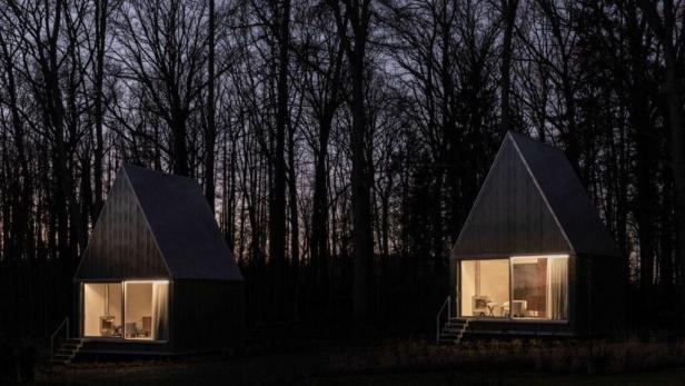 Zwei kleine, moderne Häuser mit Giebeldach stehen nachts in einem dunklen Wald.