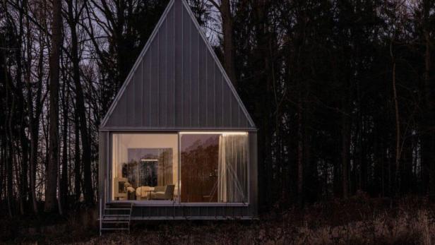 Ein kleines, modernes Haus mit Giebeldach steht im dunklen Wald.