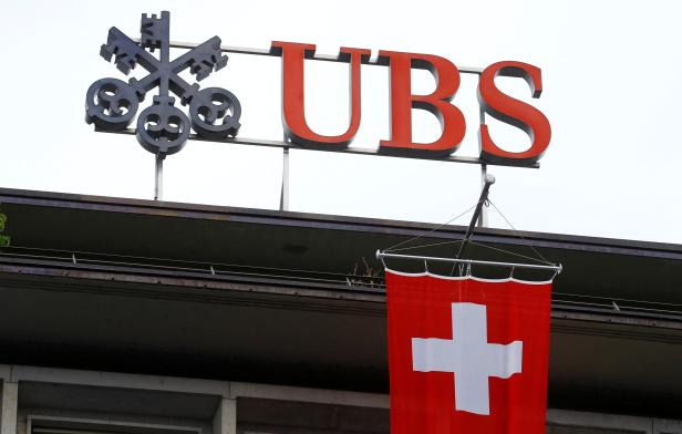 FILE PHOTO: Switzerland's national flag flies below a logo of Swiss bank UBS in Zurich