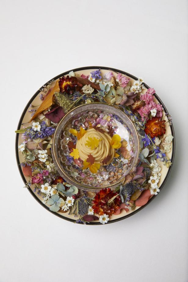 Ein Dessert in einer Glasschale, umgeben von getrockneten Blumen auf einem Teller.