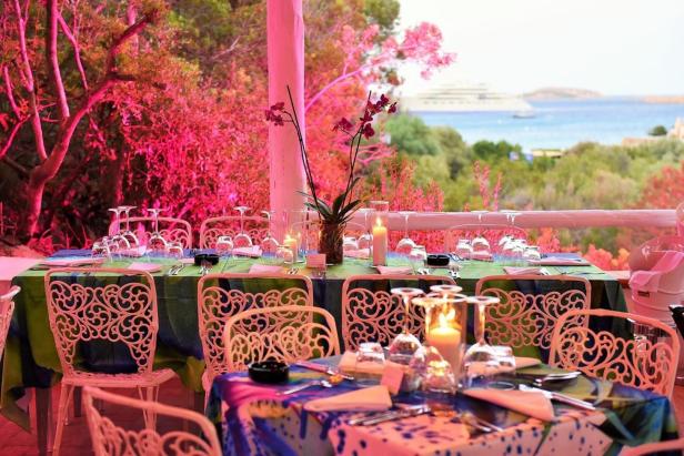 Ein gedeckter Tisch mit Gläsern und Kerzen auf einer Terrasse mit Blick auf das Meer.