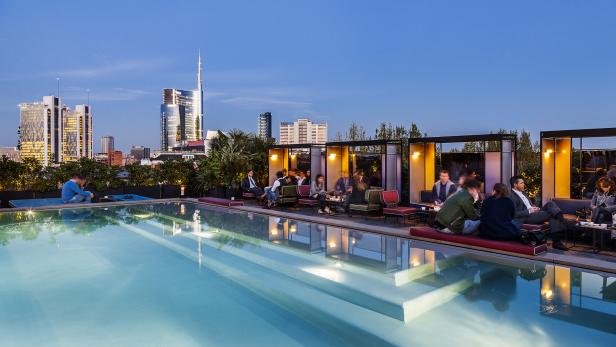 Menschen sitzen am Pool auf einer Dachterrasse mit Blick auf die Skyline von Mailand.