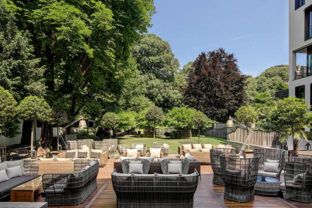 Eine Terrasse mit Korbmöbeln unter grünen Bäumen an einem sonnigen Tag.