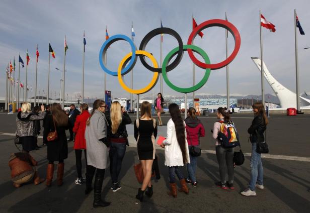 Eine Gruppe von Menschen steht vor den olympischen Ringen und Flaggen.
