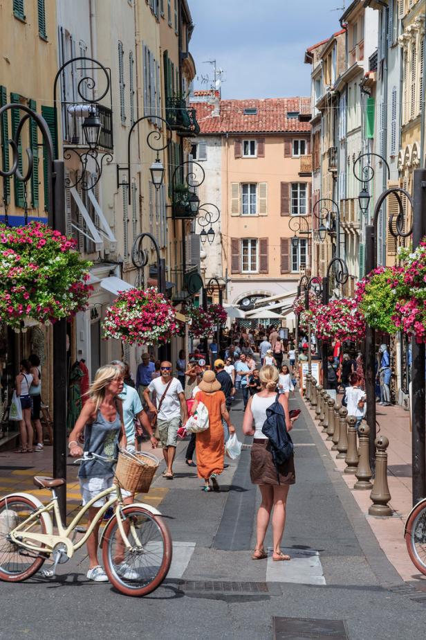 Eine belebte Straße mit Fußgängern und Blumenampeln in einer europäischen Stadt.