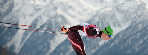 Ein Langläufer in voller Montur vor einer verschneiten Bergkulisse.
