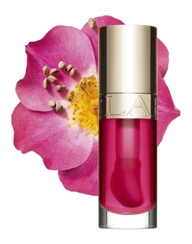 Ein rosafarbenes Clarins-Lippenöl steht vor einer rosa Blüte.