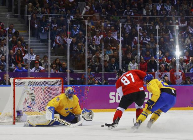 Ein Eishockeyspieler in Rot versucht, den Puck am schwedischen Torwart vorbeizuschießen.