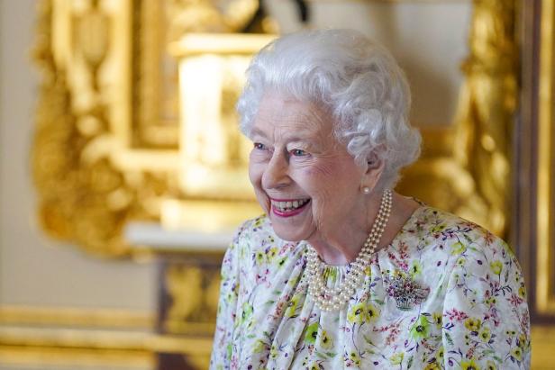 Königin Elisabeth II. lächelt in einem floralen Kleid und einer Perlenkette.