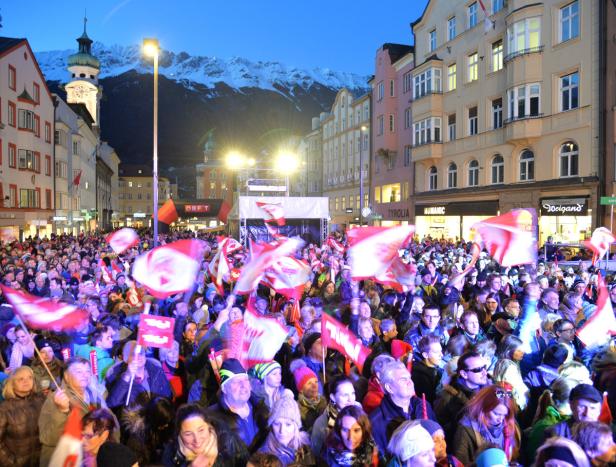 Eine Menschenmenge mit österreichischen Flaggen auf einer Straße in Innsbruck.