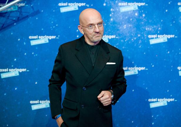 Ein Mann mit Brille und Anzug vor einem Hintergrund des Axel-Springer-Awards.