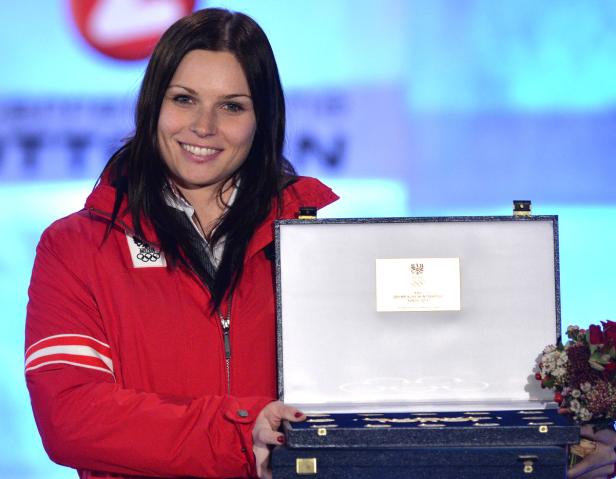 Eine Frau in roter Jacke hält eine Schatulle mit dem Logo der Olympischen Winterspiele Sotschi 2014.