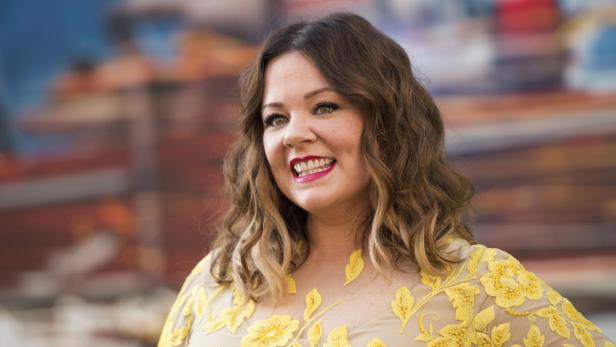 Melissa McCarthy lächelt in einem Kleid mit gelben Blumen.