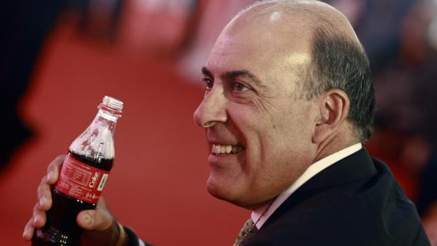 Ein lächelnder Mann im Anzug hält eine geöffnete Flasche Coca-Cola.