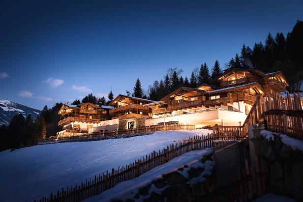 Ein luxuriöses Holzhotel liegt im Schnee unter einem dunklen Abendhimmel.