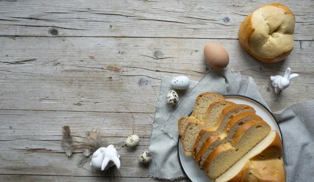 Ein Osterbrot, Eier und kleine Hasenfiguren auf einem Holztisch.