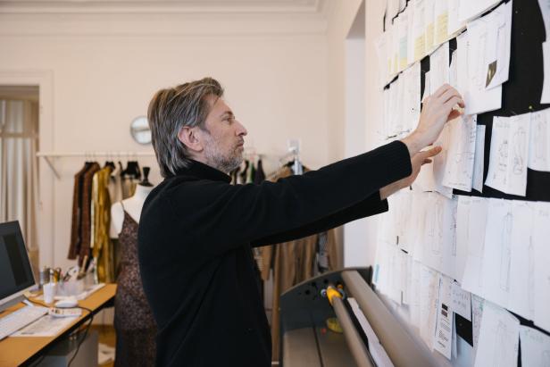 Ein Modedesigner betrachtet Skizzen an einer Wand in seinem Atelier.