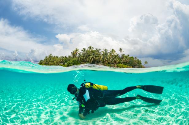 Ein Taucher schwimmt im türkisfarbenen Wasser vor einer tropischen Insel.