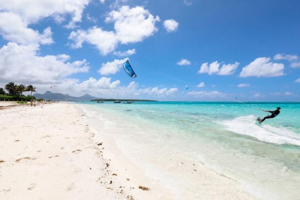 Ein Kitesurfer fährt auf einer tropischen Insel über das türkisfarbene Wasser.