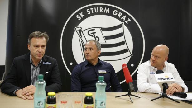 Drei Männer sitzen an einem Tisch vor dem Logo des SK Sturm Graz.