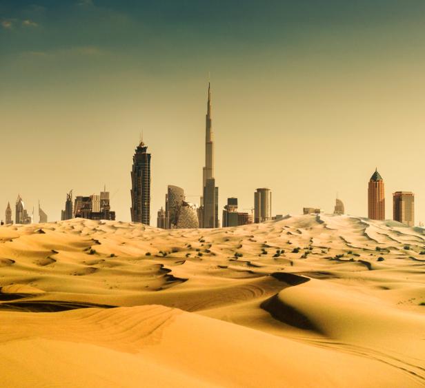 Die Skyline von Dubai erhebt sich hinter einer Sanddüne.