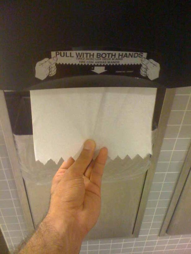 Eine Hand zieht ein Blatt Papier aus einem Spender mit der Aufschrift „Pull with both hands“.