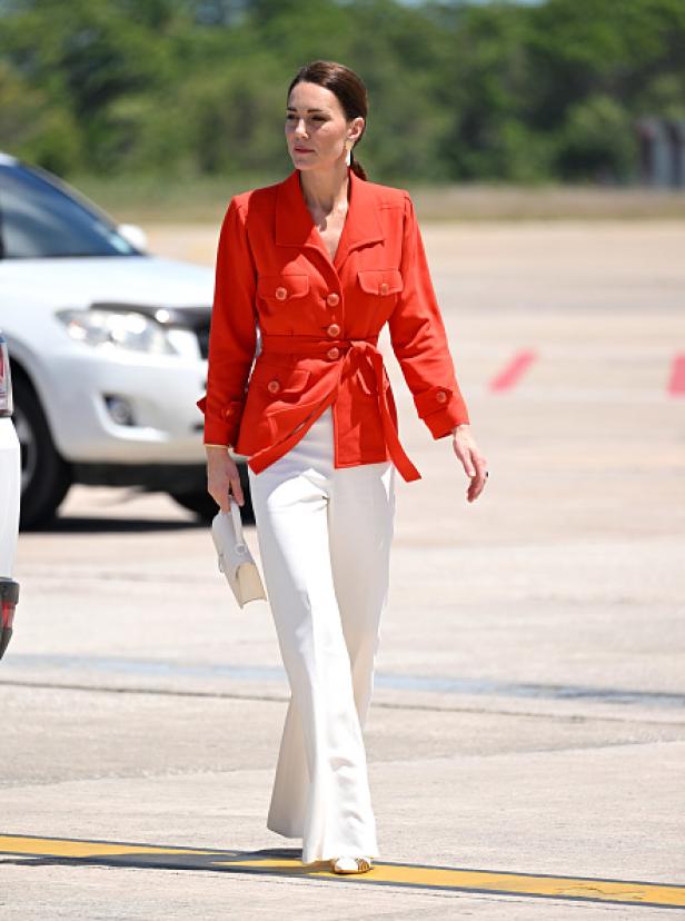 Kate Middleton in einer orangefarbenen Jacke und weißen Hosen.