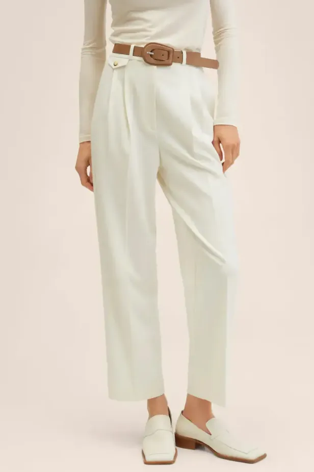 Eine Frau trägt eine weiße Hose mit braunem Gürtel und weiße Loafer.